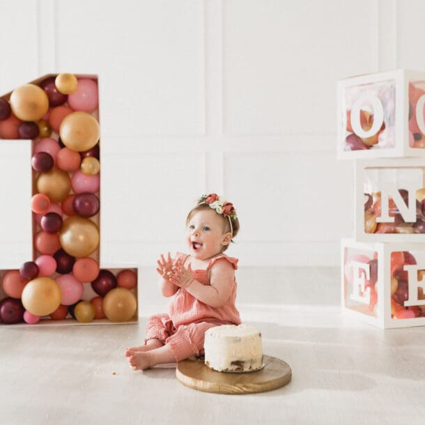 a baby sitting in front of a number and a cake. Event Photography By Bushel + Peck Photo