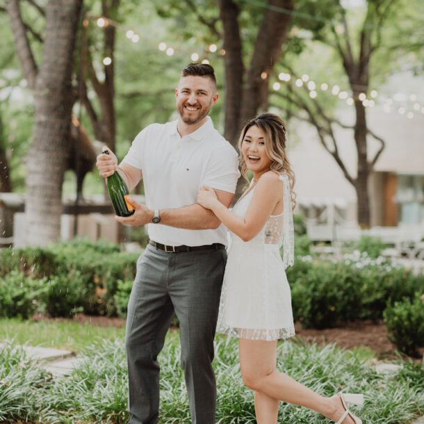 a man and woman standing in front of trees and a bottle of champagne. Photography Services By Bushel + Peck Photo