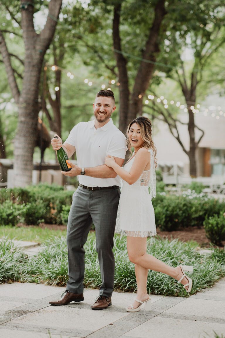 a man and woman standing in front of trees and a bottle of champagne. Photography Services By Bushel + Peck Photo