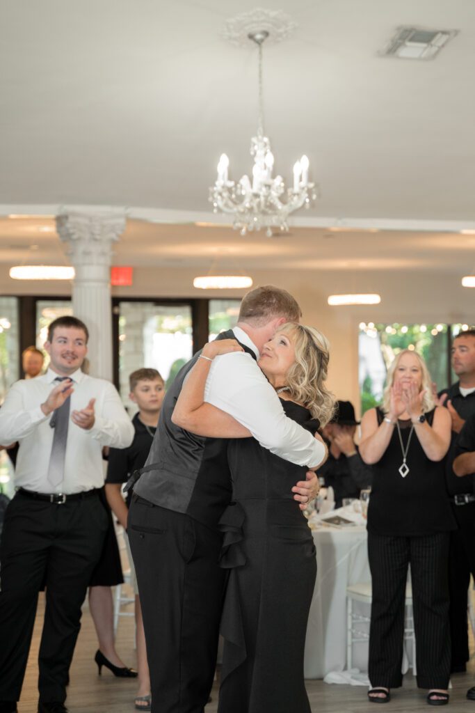 Groom hugging his mom at the end of their mother-son dance as guests applaud at Brighton Abbey, captured by Bushel + Peck Photo