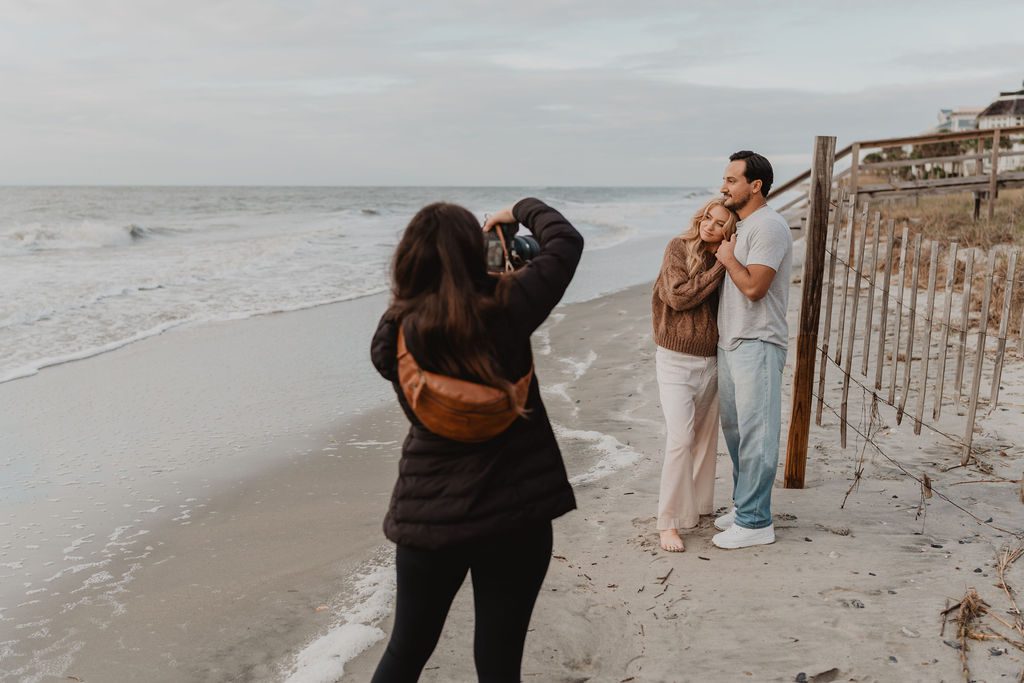 a woman taking a picture of a man and woman on a beach