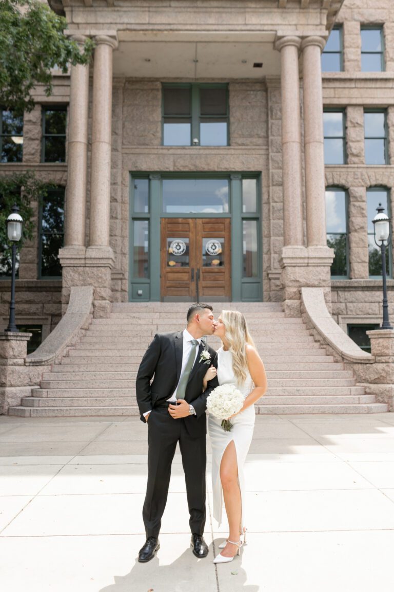 Bride and groom sharing a kiss outside the Tarrant County Courthouse during their Fort Worth courthouse elopement photographed by Bushel + Peck Photo