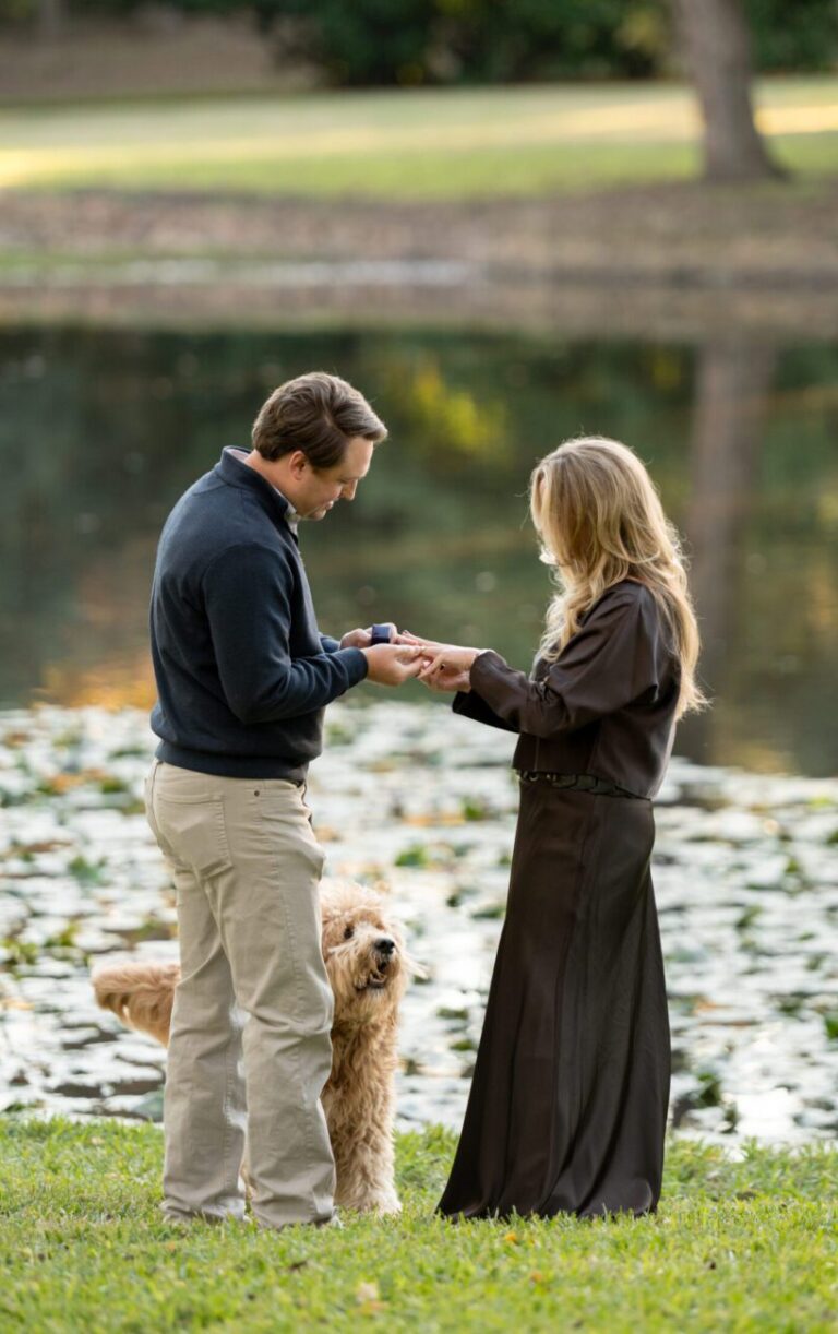 Proposal photo of couple holding hands, exchanging rings at lakeside park. captured by Bushel + Peck Photo