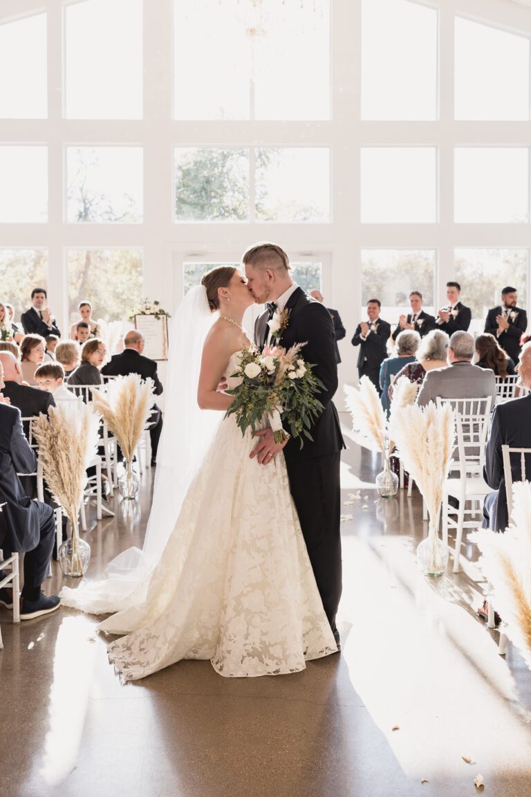 bride and groom first kiss as the come down Thea aisle at The Farmhouse Venue in Montgomery,TX near Houston. Captured by Bushel + Peck Photo