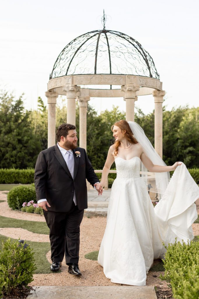 Bride and groom holding hands beneath the garden gazebo at Knotting Hill Place in Frisco, captured by Bushel + Peck Photo
