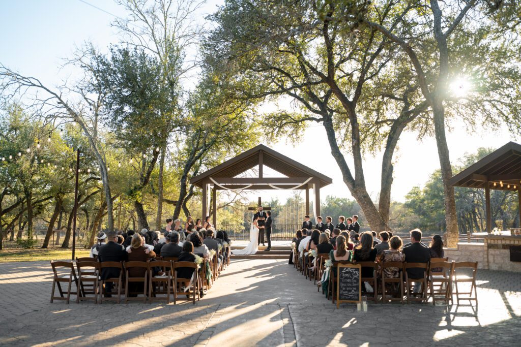 Guests seated for an outdoor wedding ceremony beneath the oak trees at The Ranch Austin, captured by Bushel + Peck Photo