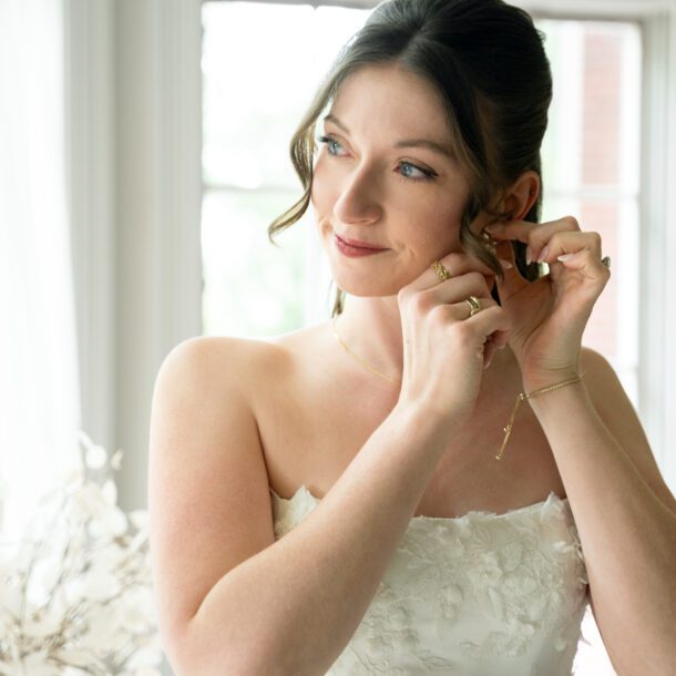 Bride putting on earrings during wedding day preparations photographed by Bushel + Peck Photo.