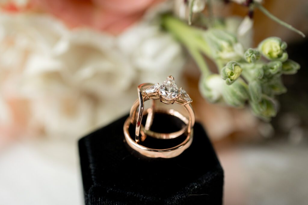 Close-up of a wedding ring set resting on a black ring box beside white flowers, captured by Bushel + Peck Photo
