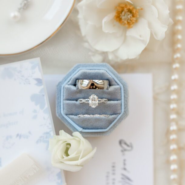 Wedding rings in a dusty blue ring box with florals and invitation details at a Fort Worth wedding — Bushel + Peck Photo Fort Worth wedding photographer