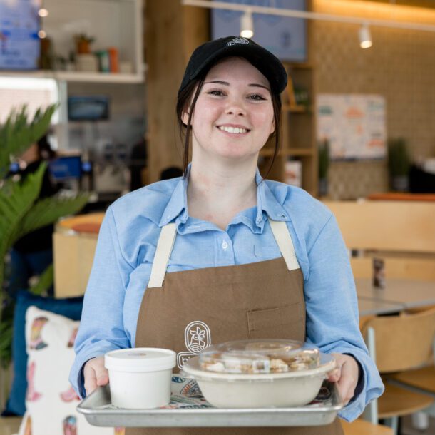 Smiling Birdcall team member holding a tray of food at the restaurant's grand opening in McKinney, Texas, captured by Bushel + Peck Photo.