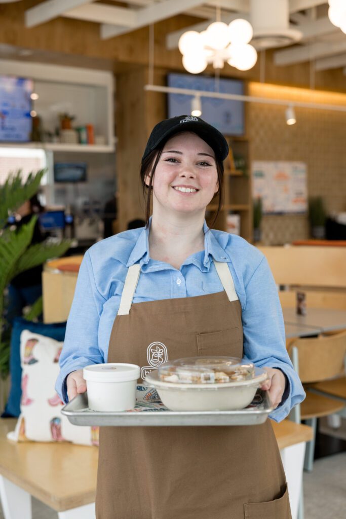 Smiling Birdcall team member holding a tray of food at the restaurant's grand opening in McKinney, Texas, captured by Bushel + Peck Photo.