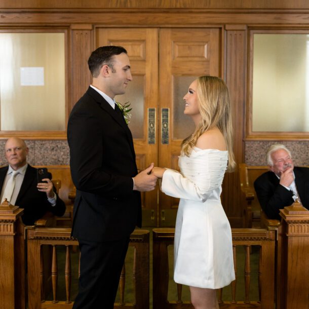 Bride and groom facing each other during their vows in the historic Tarrant County courtroom as family looks on, captured by Bushel + Peck Photo