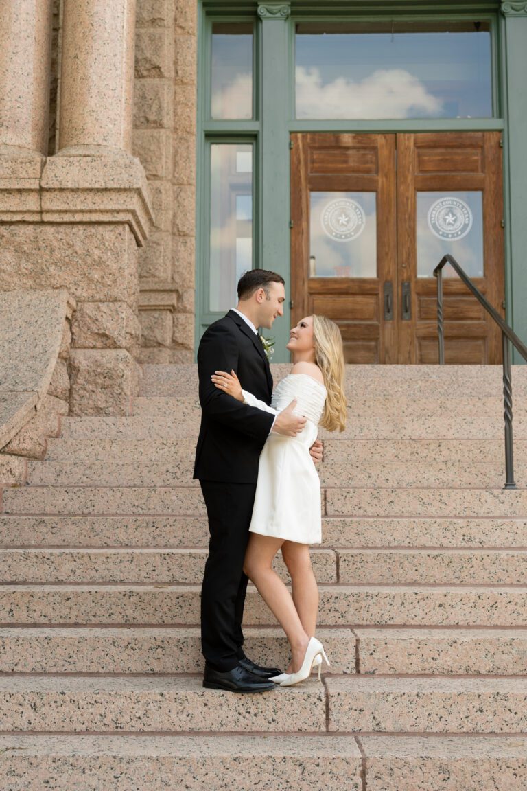 Couple embracing on the pink granite steps of the Tarrant County Courthouse, captured by Bushel + Peck Photo