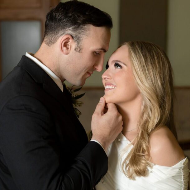 Groom gently holding his bride’s face in a warmly lit hallway of the Tarrant County Courthouse, captured by Bushel + Peck Photo