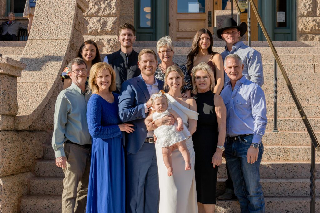 Newlyweds holding their baby daughter with their extended family on the granite steps of the Tarrant County Courthouse, captured by Bushel + Peck Photo
