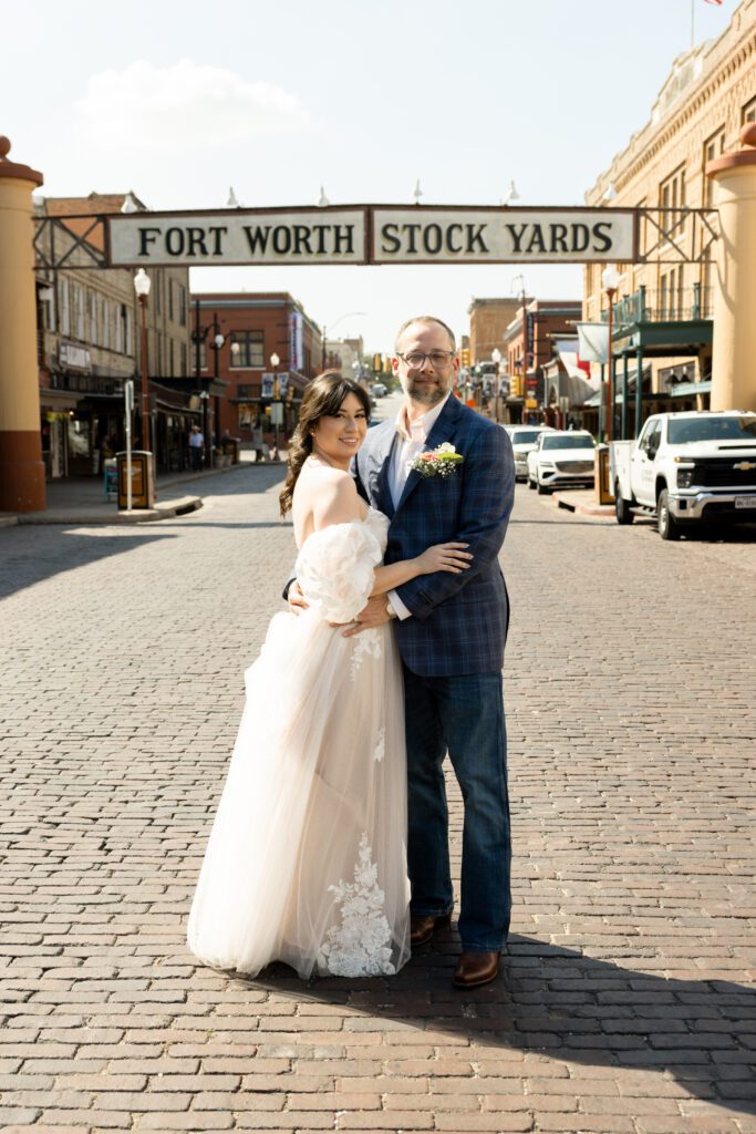 Bride and groom standing together on the brick street beneath the Fort Worth Stockyards sign after their Tarrant County Courthouse wedding, captured by Bushel + Peck Photo