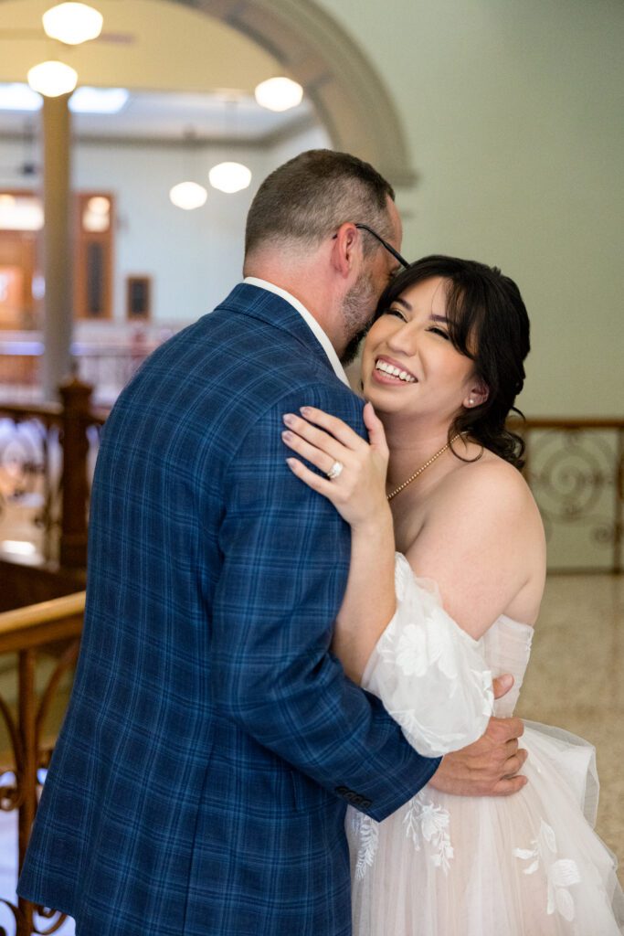 Groom embracing his bride cheek to cheek in a hallway of the Tarrant County Courthouse, captured by Bushel + Peck Photo
