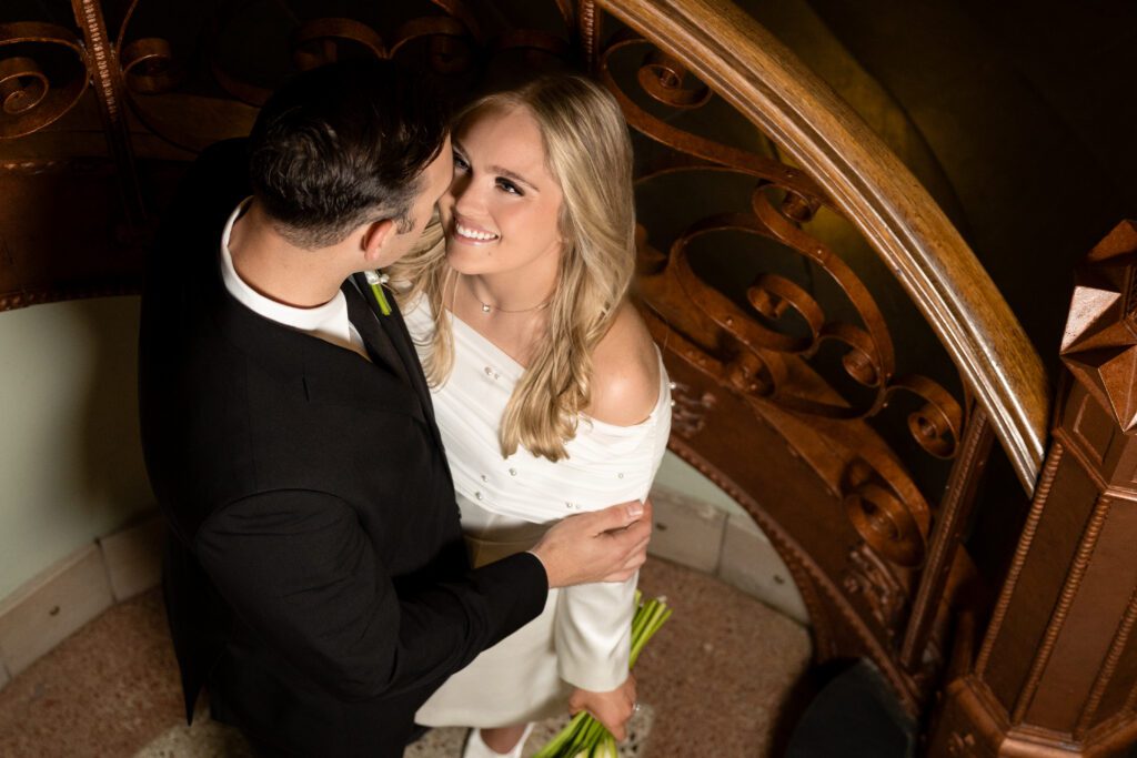 Overhead view of newlyweds embracing on the spiral staircase inside the Tarrant County Courthouse, captured by Bushel + Peck Photo