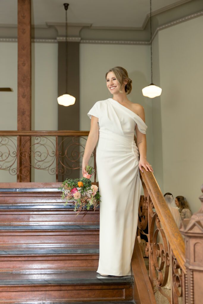 Bride standing on the carved wooden staircase inside the historic Tarrant County Courthouse, captured by Bushel + Peck Photo