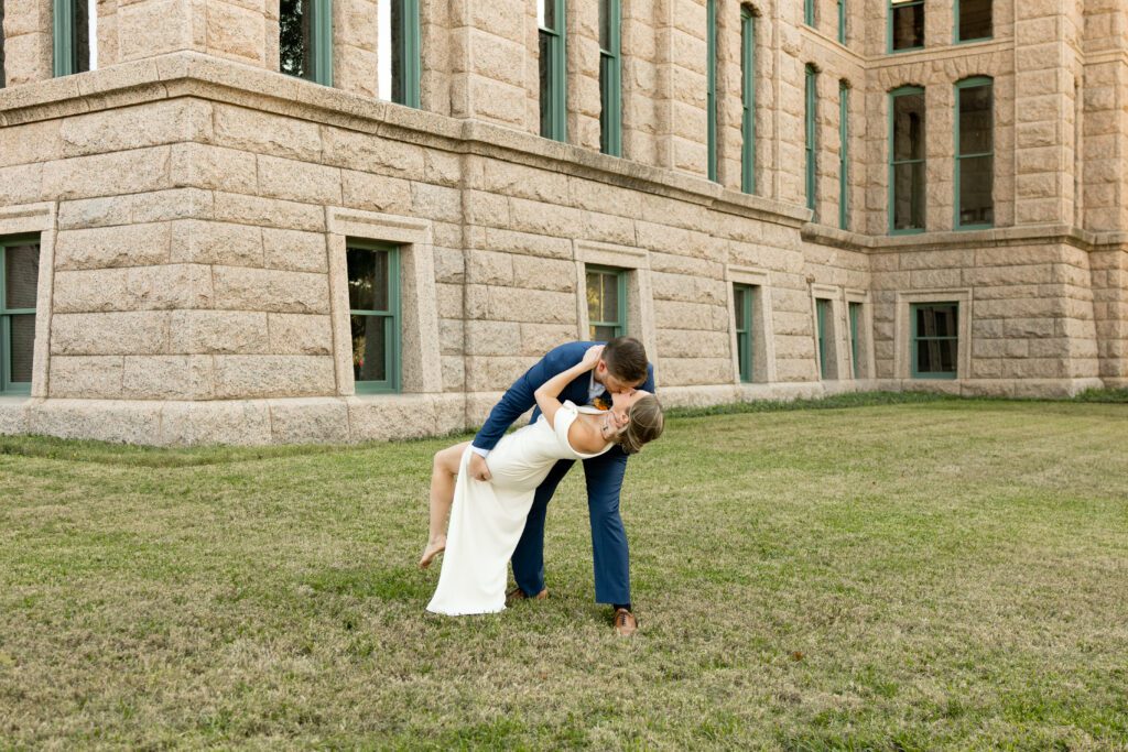 Groom dipping his bride on the lawn beside the Tarrant County Courthouse, captured by Bushel + Peck Photo