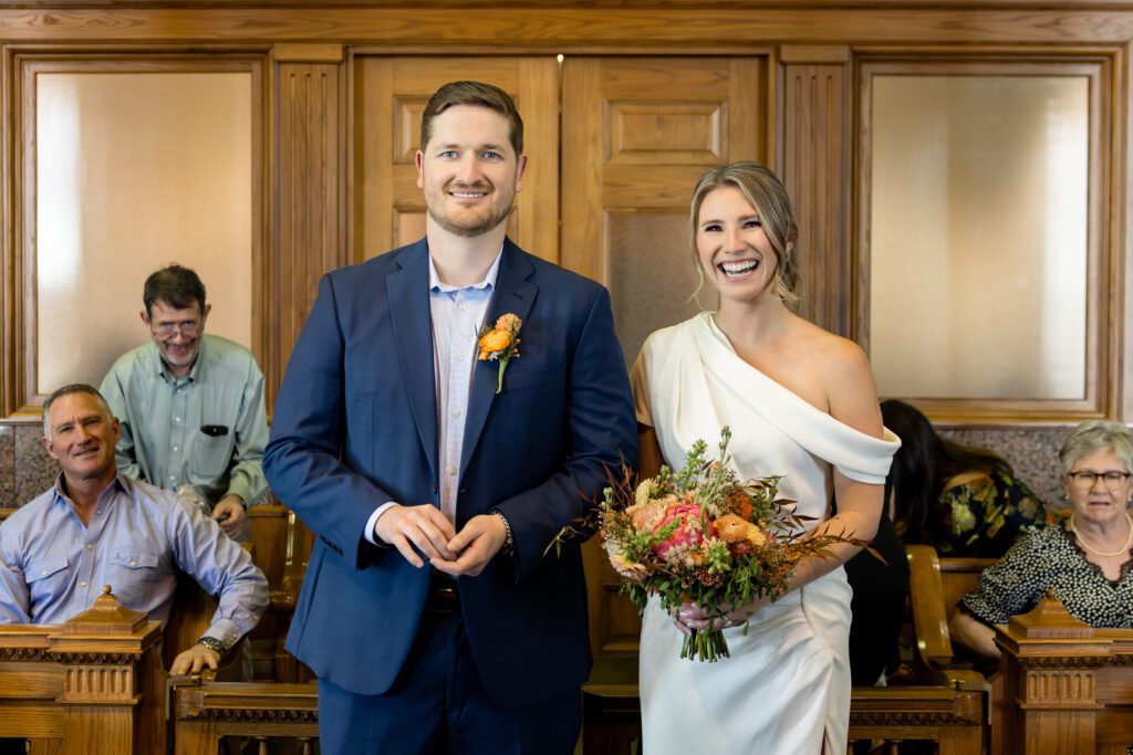 Smiling bride and groom standing before the judge during their Tarrant County Courthouse wedding ceremony, captured by Bushel + Peck Photo