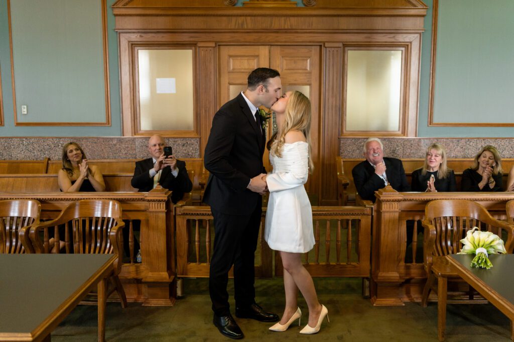 First kiss in the historic courtroom as family applauds at a Fort Worth courthouse wedding, captured by Bushel + Peck Photo