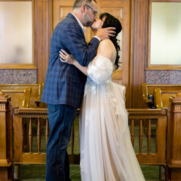 First kiss in front of the wood-paneled courtroom doors at the Tarrant County Courthouse, captured by Bushel + Peck Photo