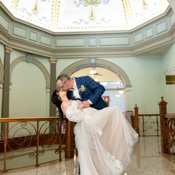 Groom dipping his bride beneath the painted dome of the Tarrant County Courthouse rotunda, captured by Bushel + Peck Photo