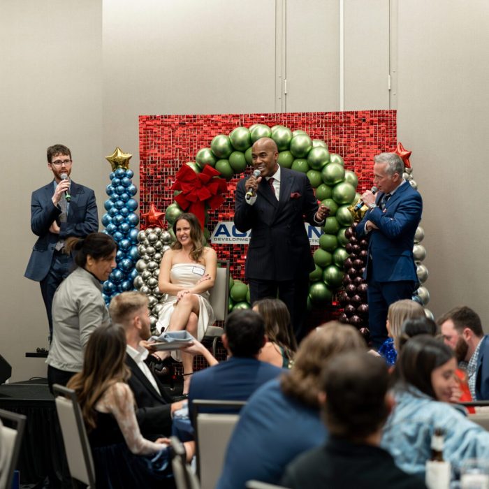 Guests seated at the Acadian corporate Christmas party with a balloon arch backdrop, captured by Bushel + Peck Photo
