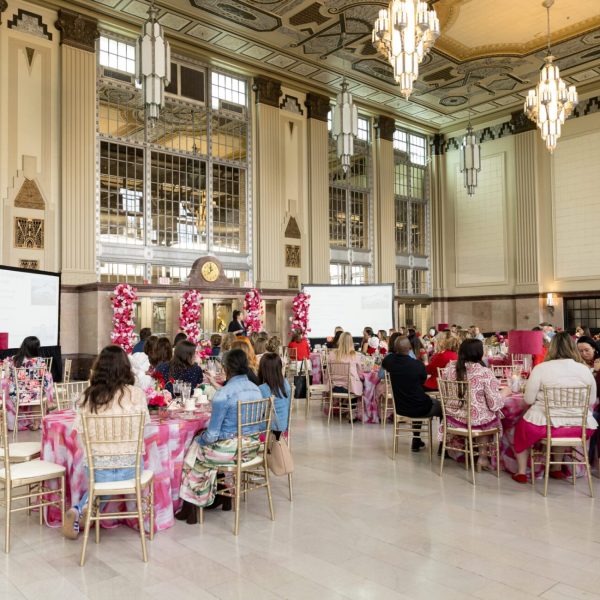 Guests seated at pink-themed tables beneath chandeliers during a Professional Wedding Guild luncheon, corporate event photography, captured by Bushel + Peck Photo