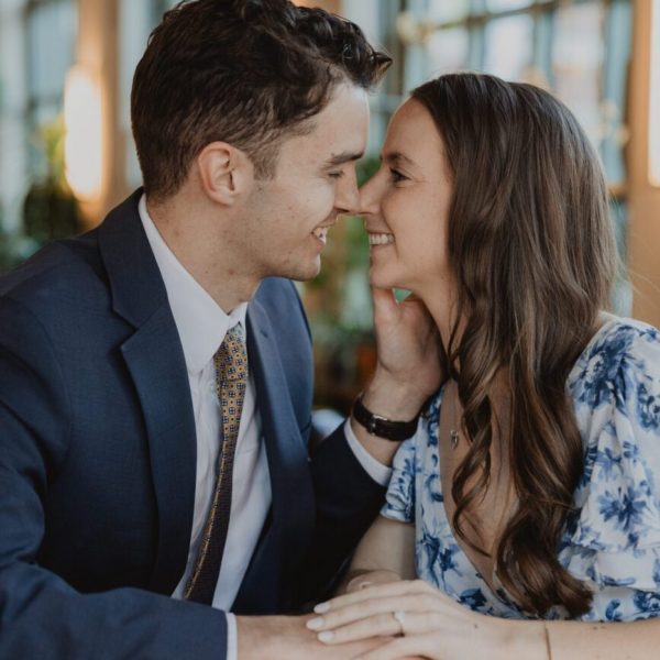 couple sitting at table faces close almost kissing during and engagement session captured by bushel + peck photo in Sundance Square in Fort Worth, TX.
