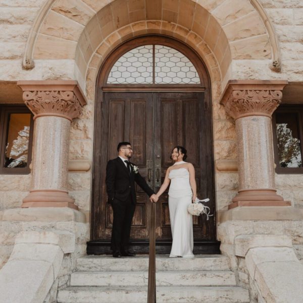 Bride and groom holding hands in the arched doorway of the historic Denton County Courthouse after their elopement, captured by Bushel + Peck Photo
