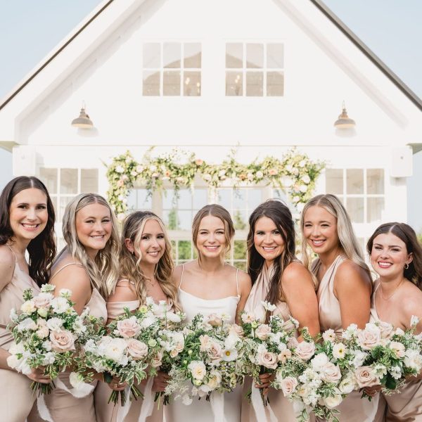 Bridesmaids posing with bouquets in front of a white barn at a Dallas & Fort Worth photography location, ideal for weddings, portraits, and corporate photography by Bushel + Peck Photo.